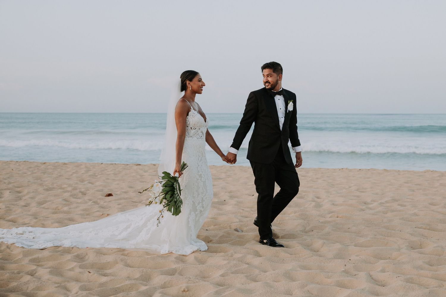 Romantic beach wedding photography session with flowing white dress against ocean backdrop.