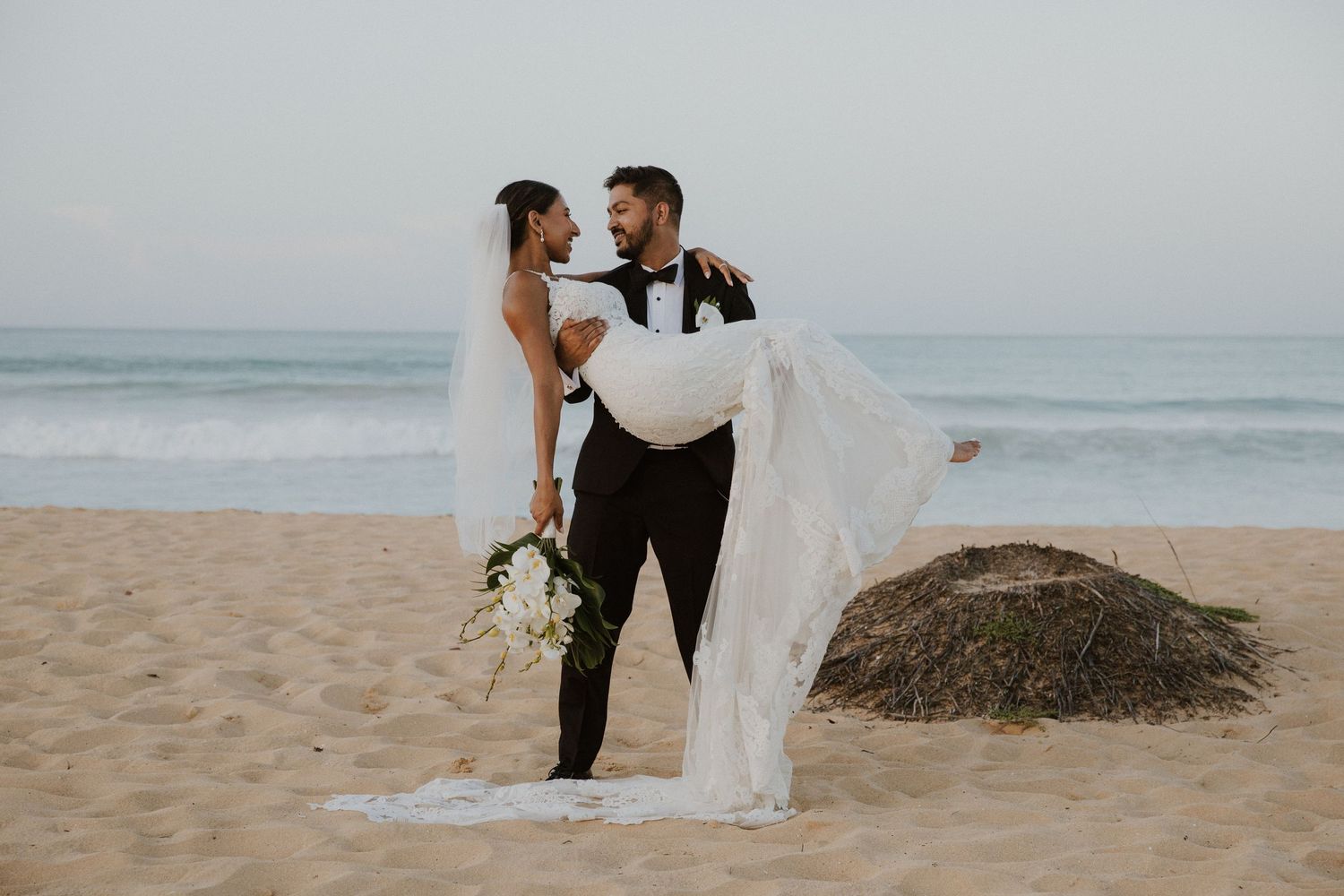 Elegant beachside wedding portraits with dramatic waves and coastal cliffs in background.