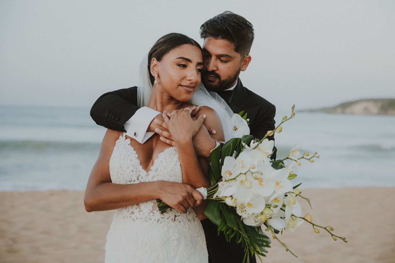 Intimate wedding photography session on sandy beach with white orchid bouquet.