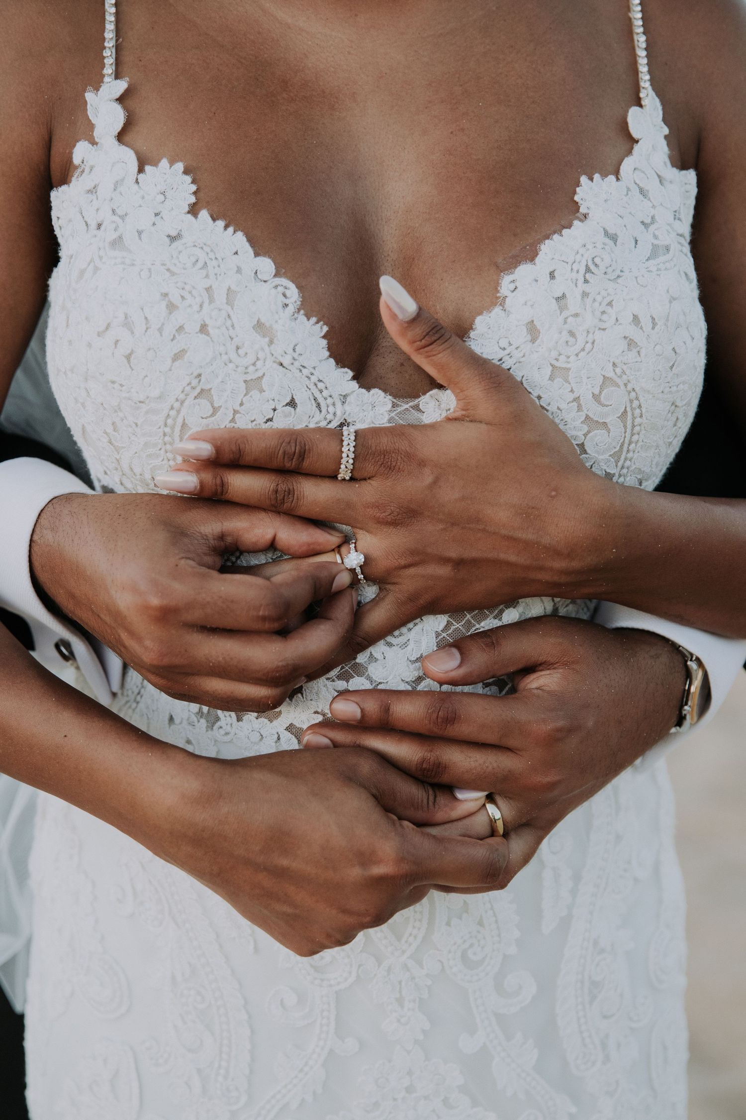Close-up of wedding rings and lace dress details during beach ceremony.