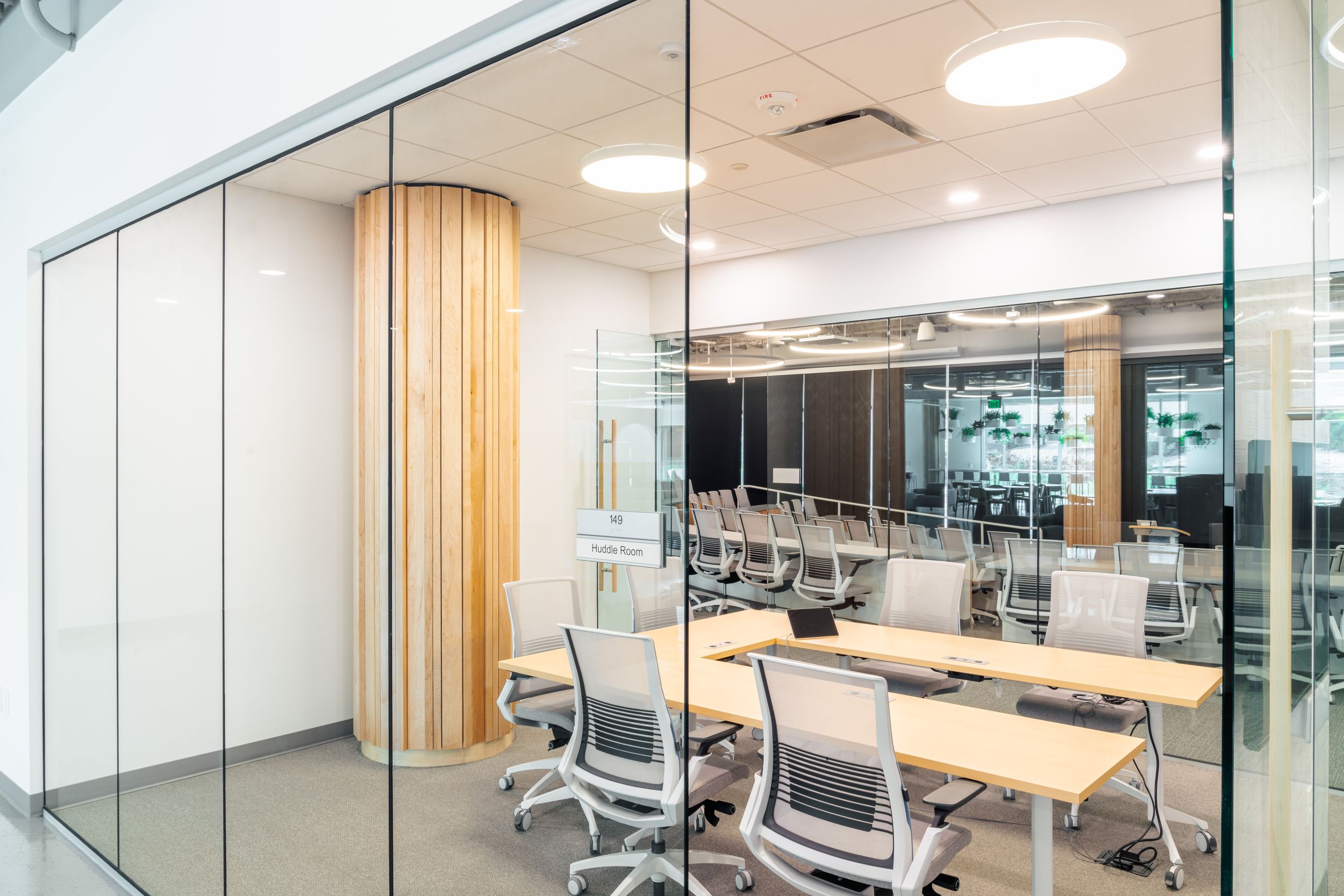 Modern office space with glass conference rooms, white desks, and ergonomic chairs under recessed lighting.