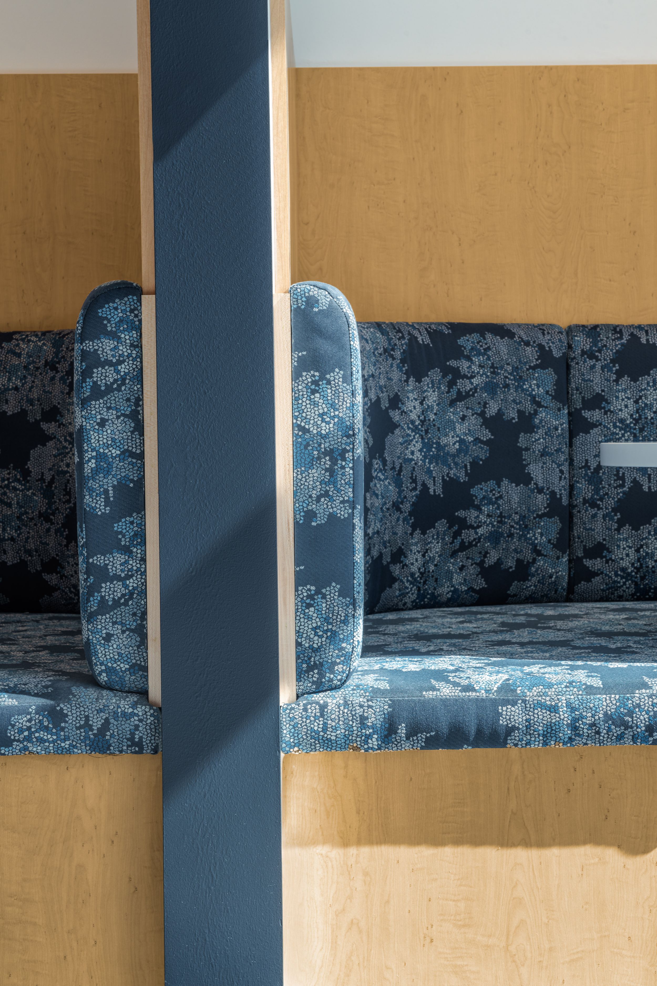Vintage blue floral patterned booth seating divided by a white pillar against yellow walls.