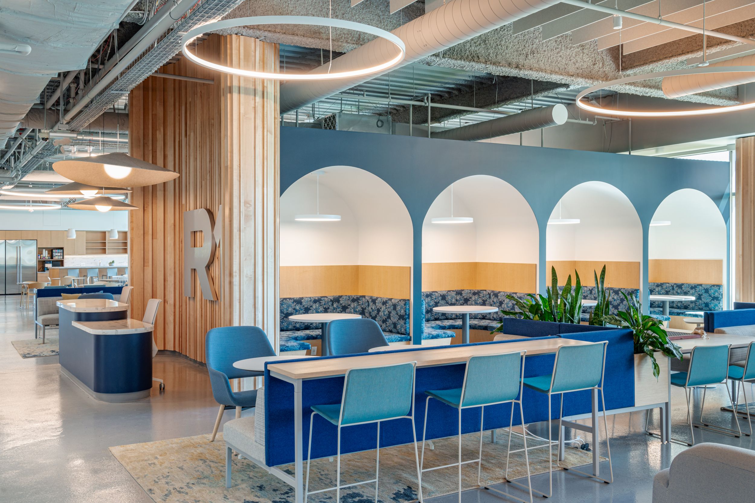 Modern office breakroom with blue barstools, arched wall alcoves, and circular pendant lighting fixtures.