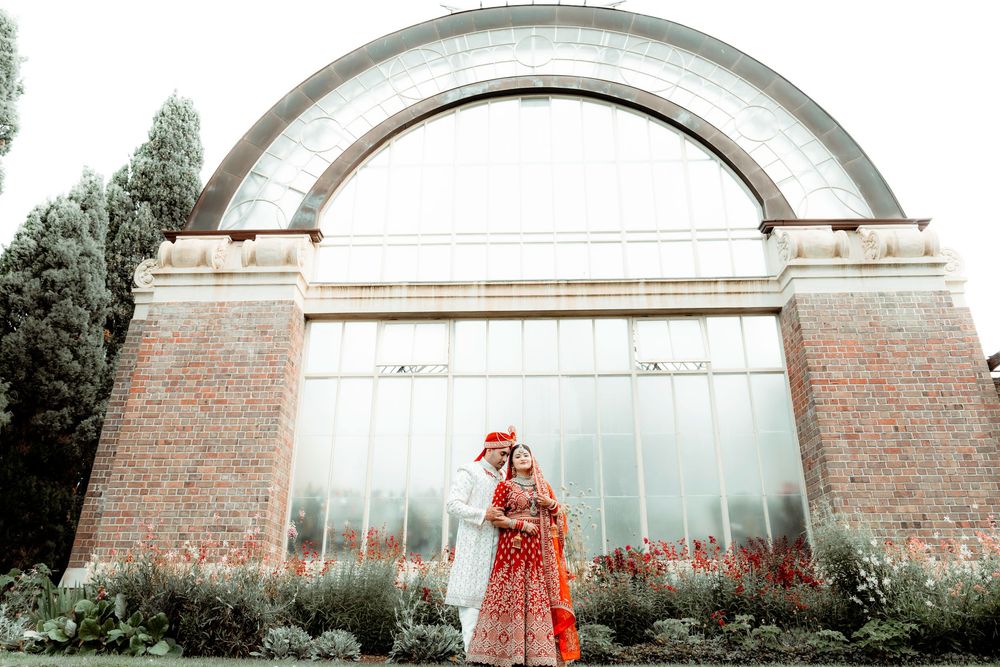 Person in a vibrant red dress poses against a rustic brick and glass greenhouse structure.