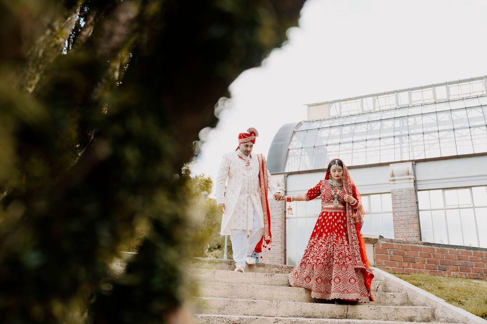 Two people in traditional Indian wedding attire walk down stone steps during an outdoor photoshoot.