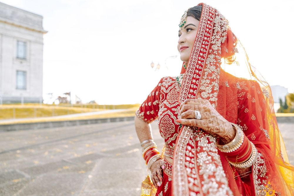 Bride in traditional red and gold Indian wedding attire poses on rooftop during sunset portraits.