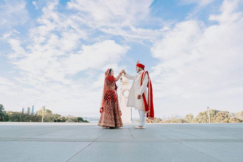 High angle beach view of wedding couple in traditional Indian attire walking along scenic coastline.