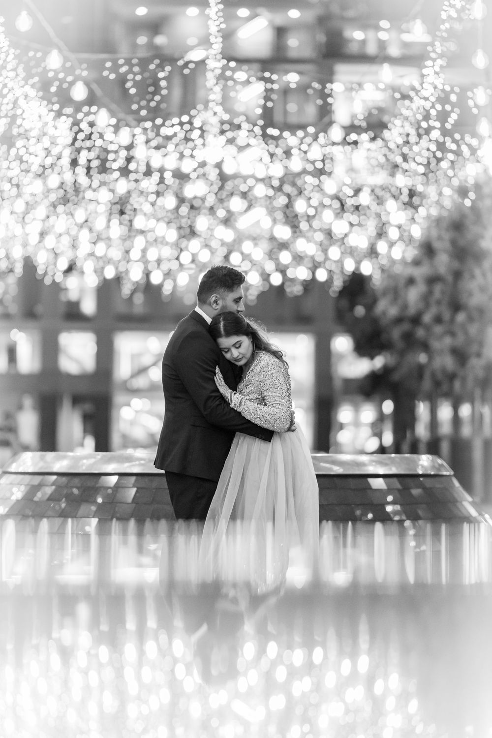 Romantic couple embracing under twinkling string lights in black and white photography.