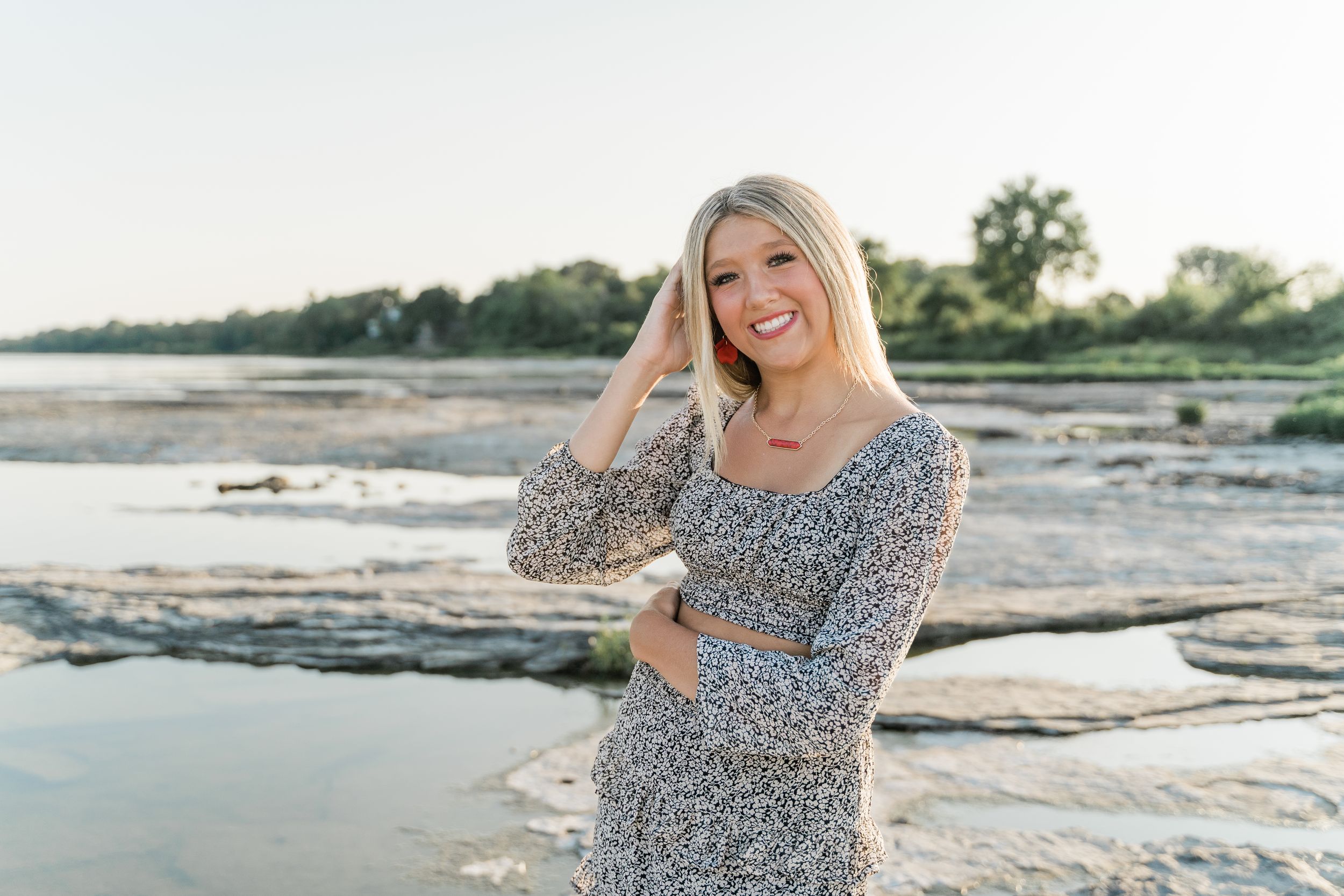 Someone walks joyfully along a rocky beach shoreline at sunset with gentle waves in the background.