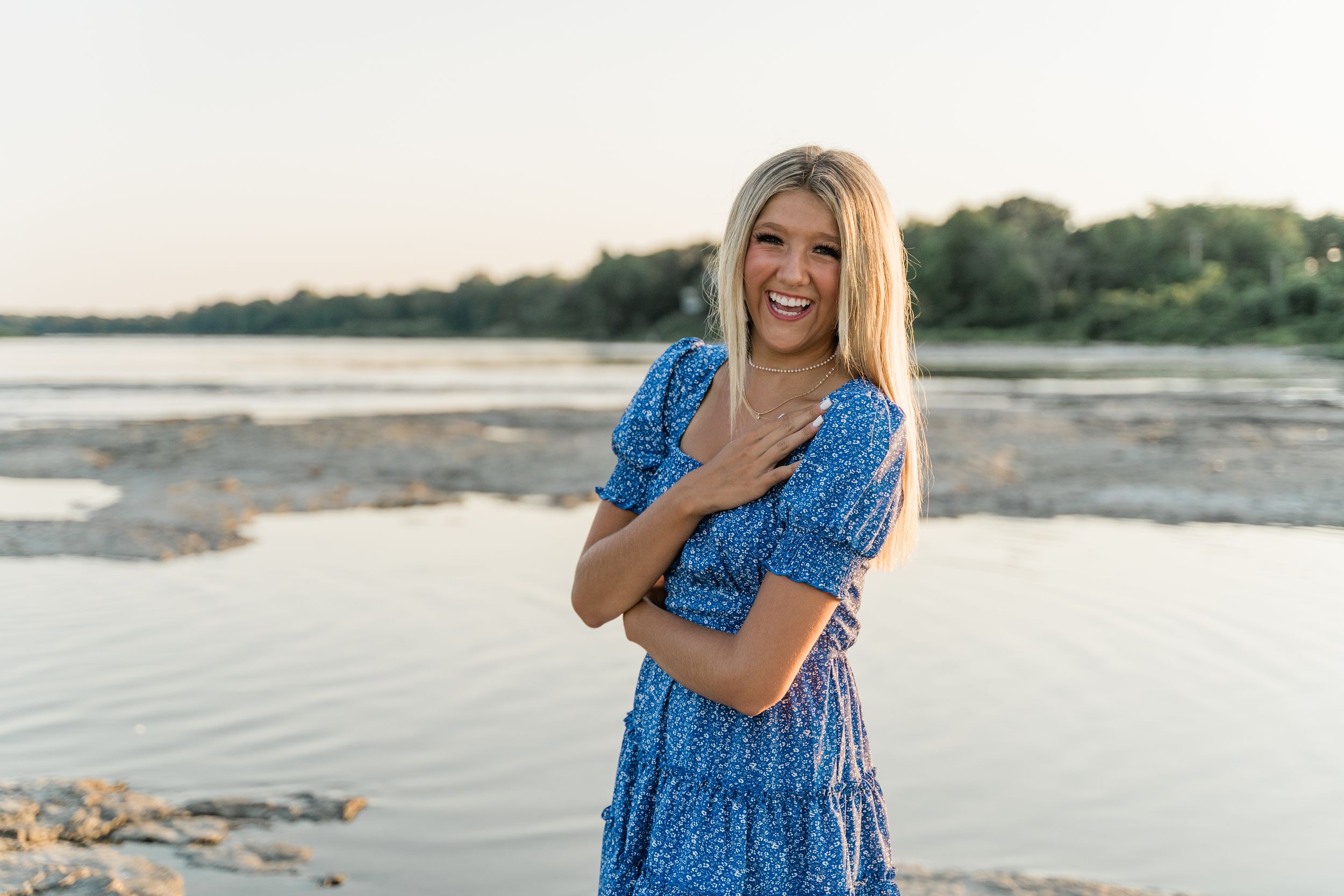 Woman in blue sundress walking along a serene beach shoreline during golden hour.