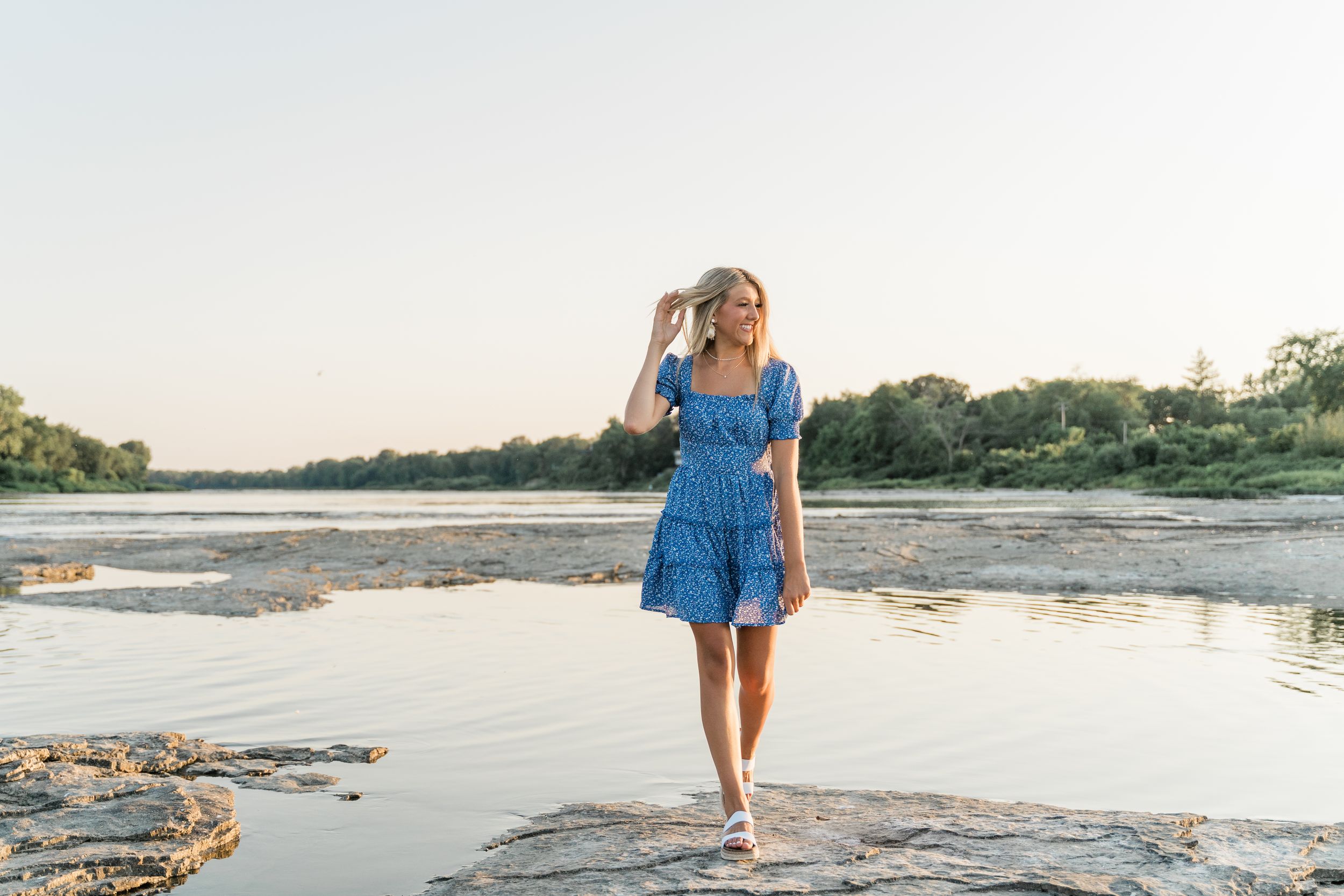 A serene coastal scene shows someone walking near the water's edge during golden hour.