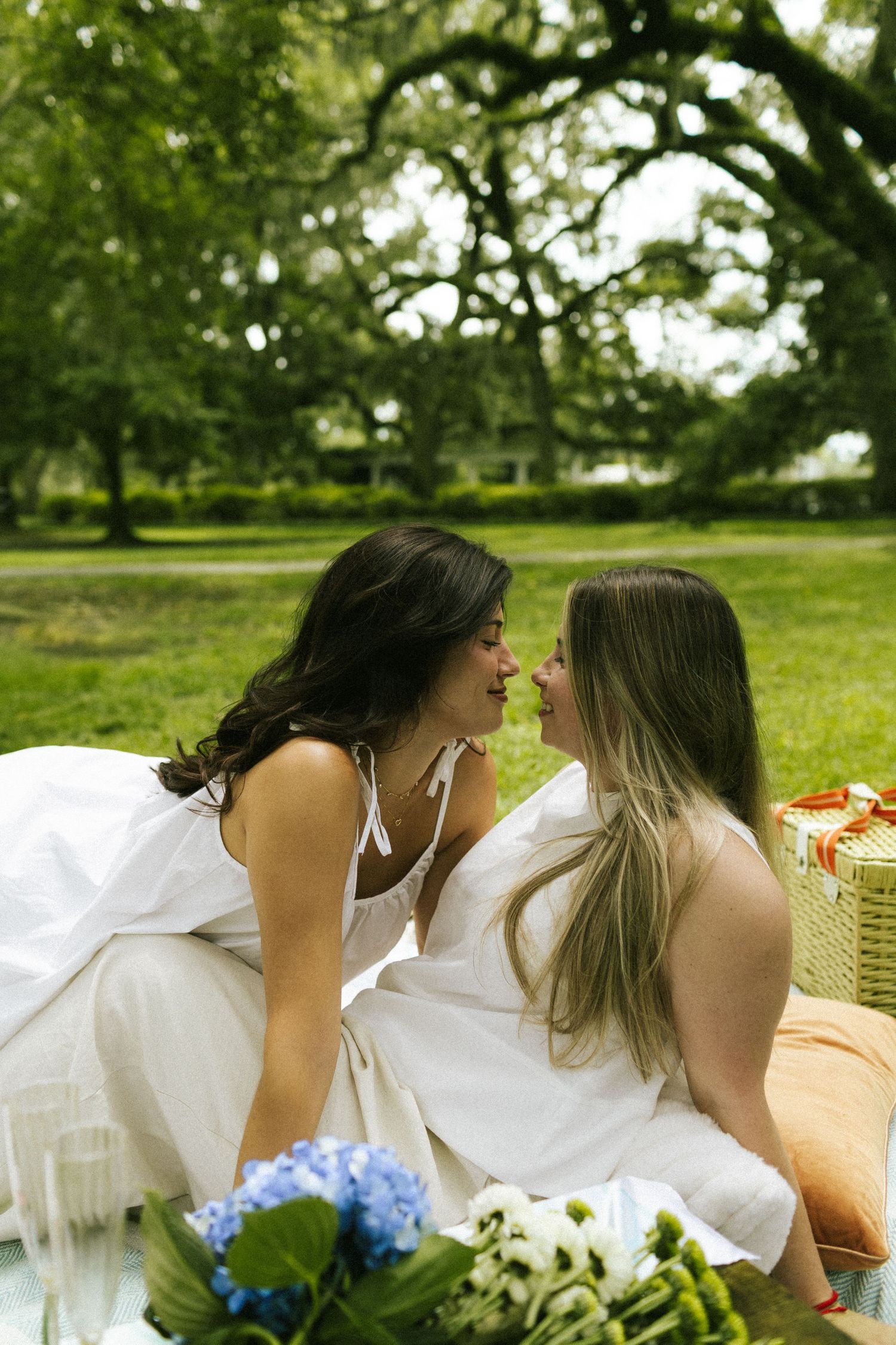 Two women on a picnic blanket in Forsyth Park, leaning over one another about to kiss
