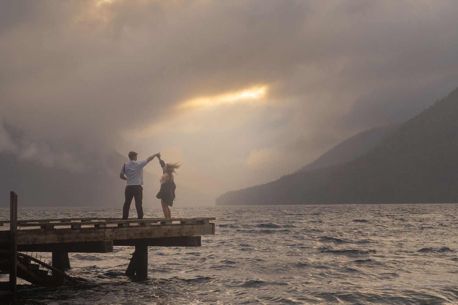 Two figures stand in a mountain meadow filled with white wildflowers at sunset.