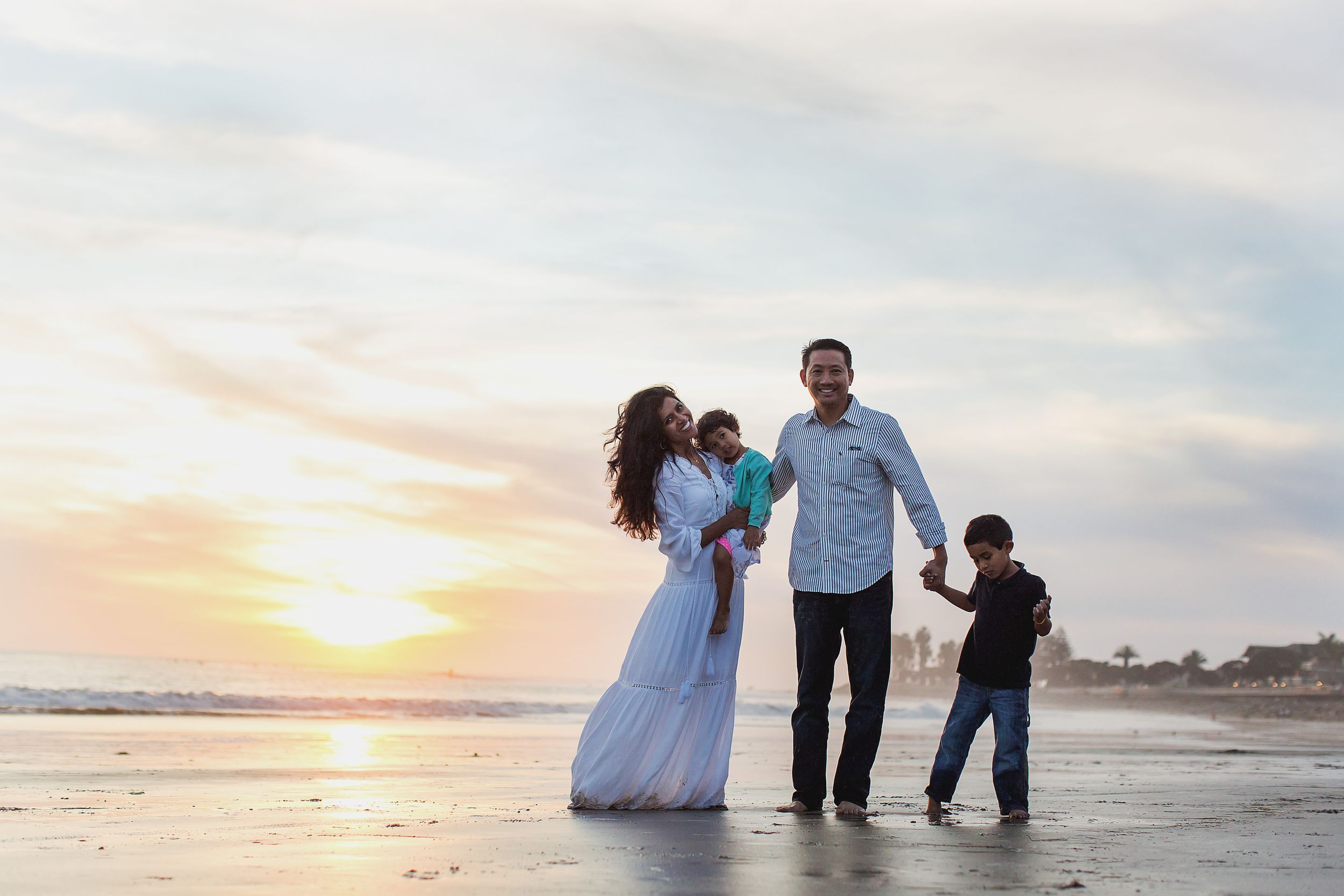 A family walks along the beach at sunset creating silhouettes against the golden sky.