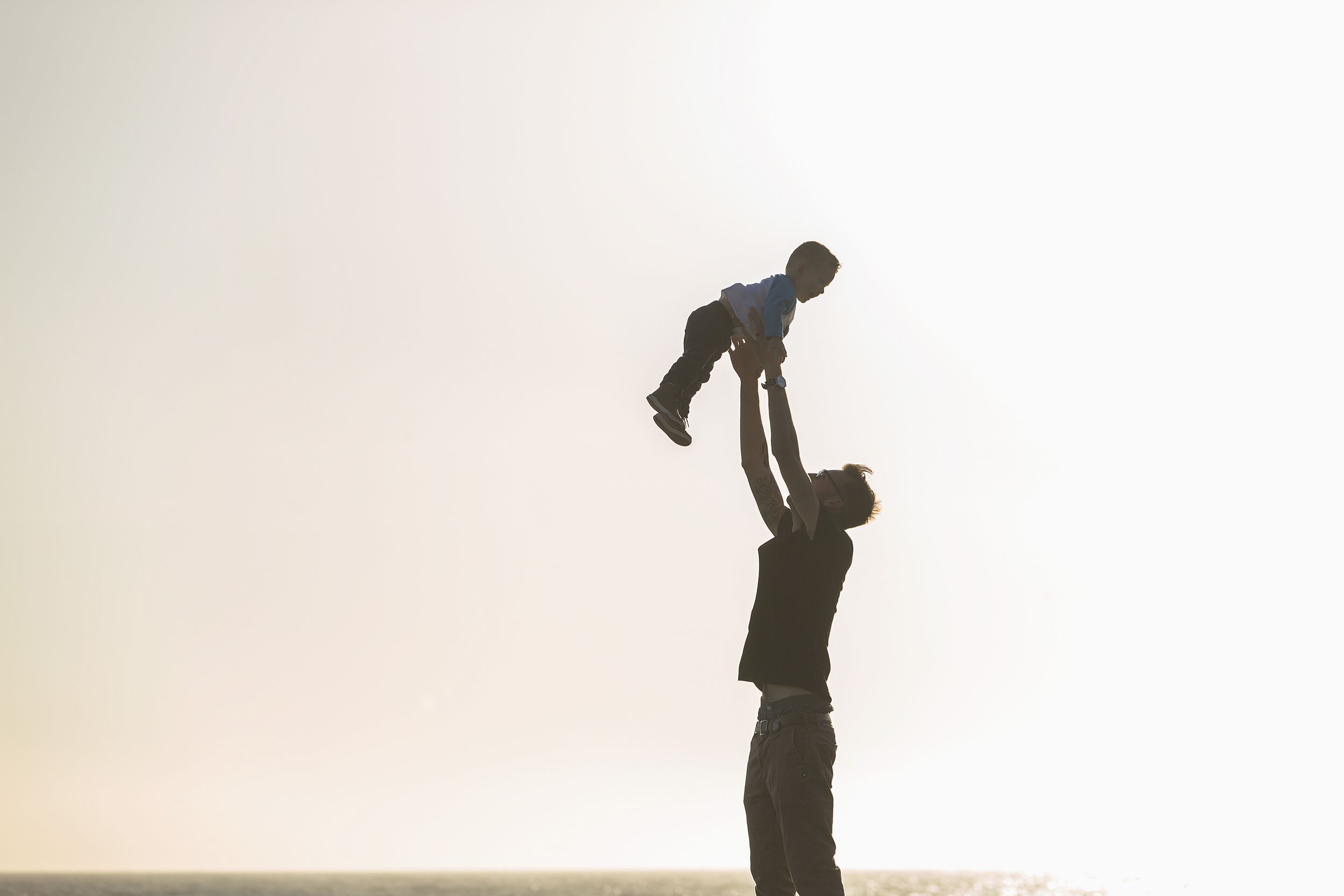 A silhouette of a parent lifting a child high in the air against a bright sky.
