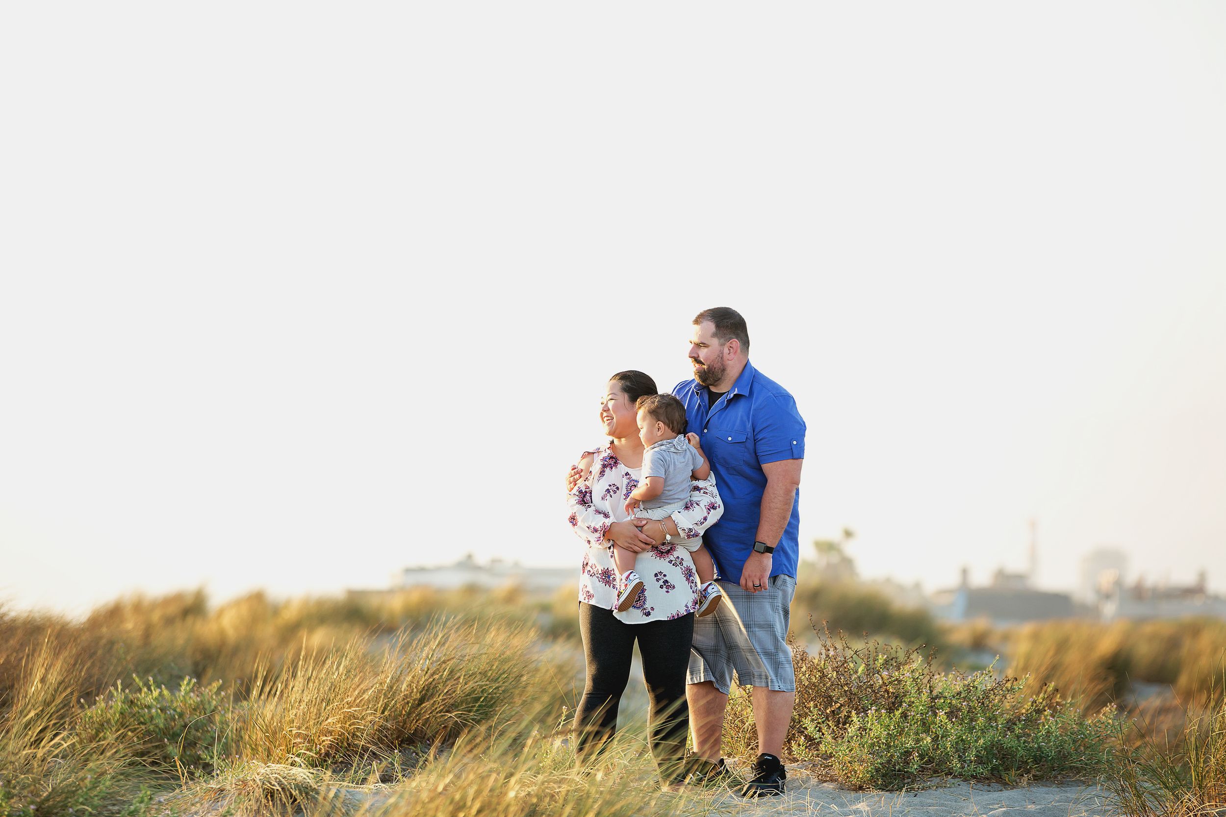 A family strolls together through tall grass at sunset near the coast.