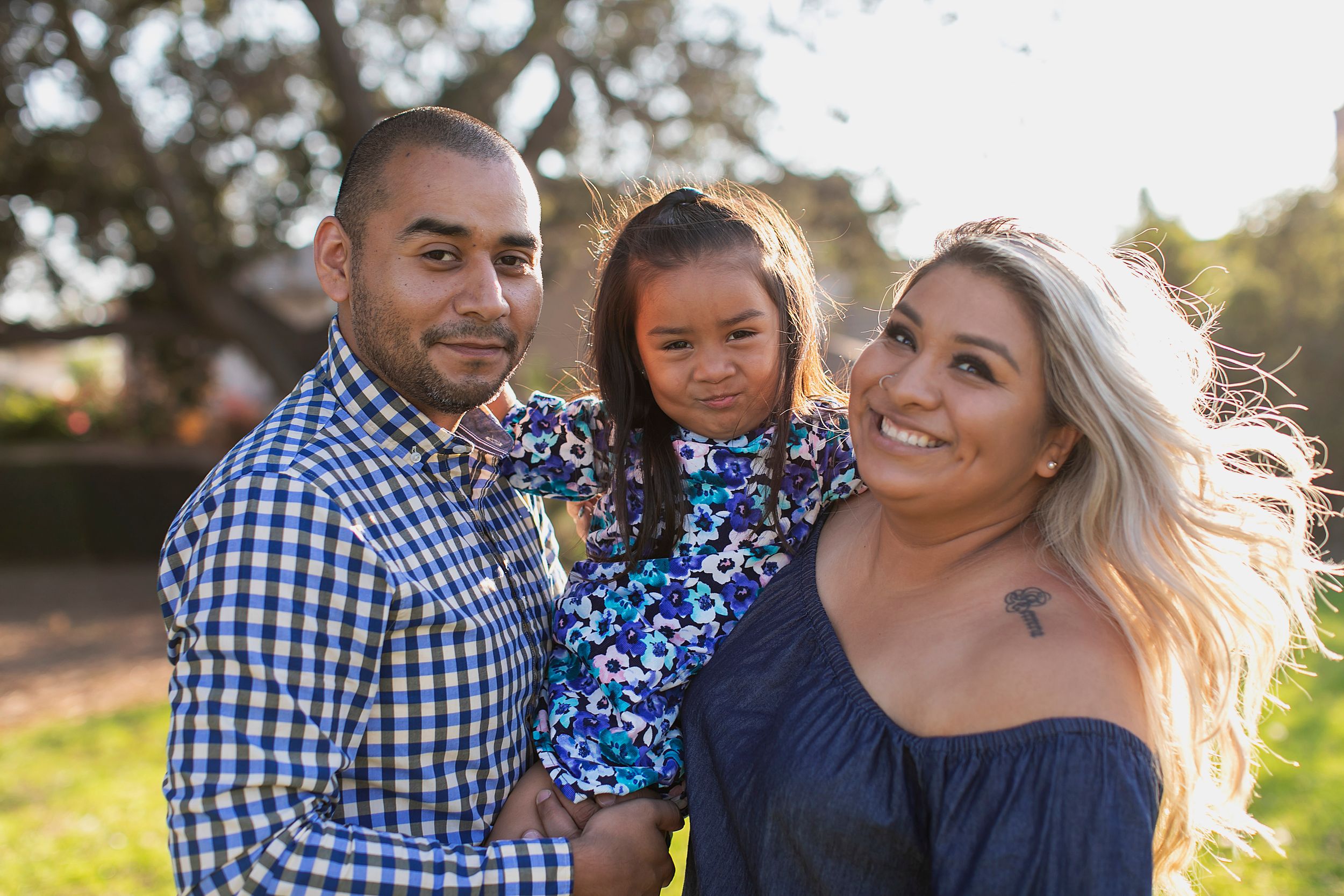A family enjoys a sunny outdoor portrait session wearing coordinated navy and blue outfits.