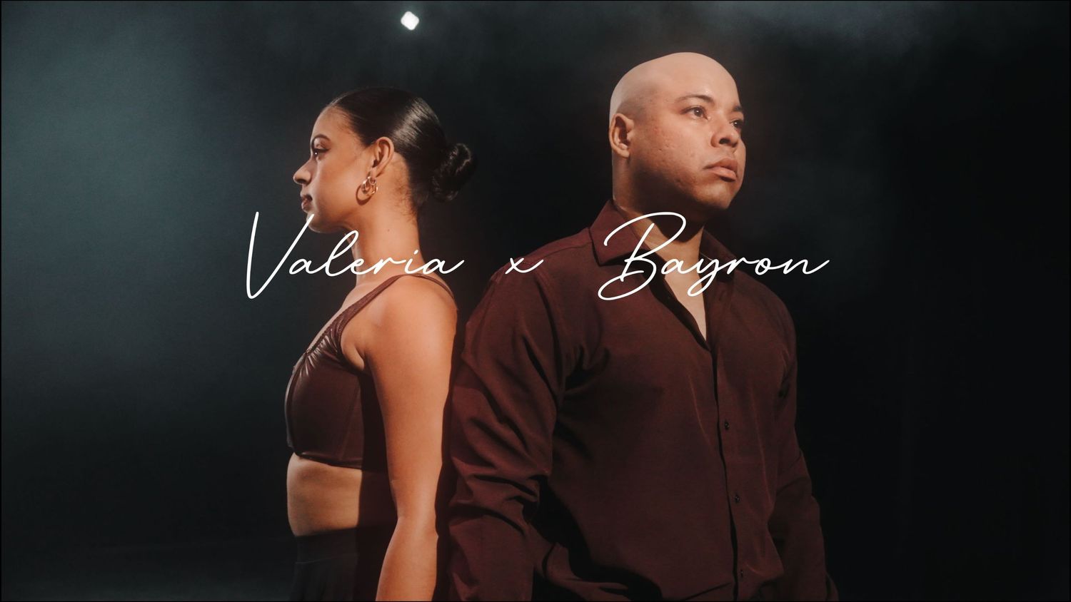 Two dancers in dark outfits perform in dramatic lighting against a moody background.