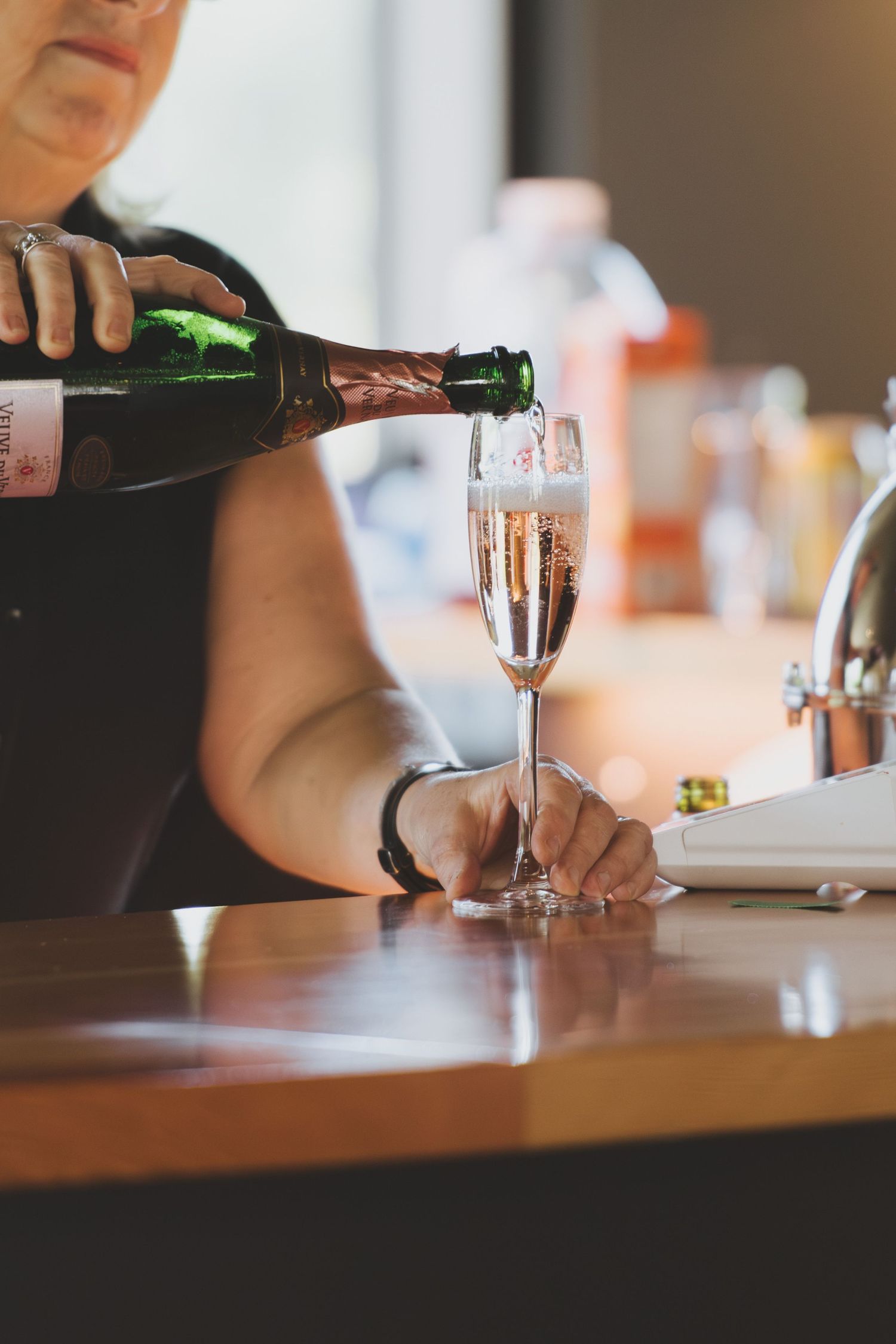 Champagne being poured into glasses at a bar showing bartender's hands in a brightly lit setting.