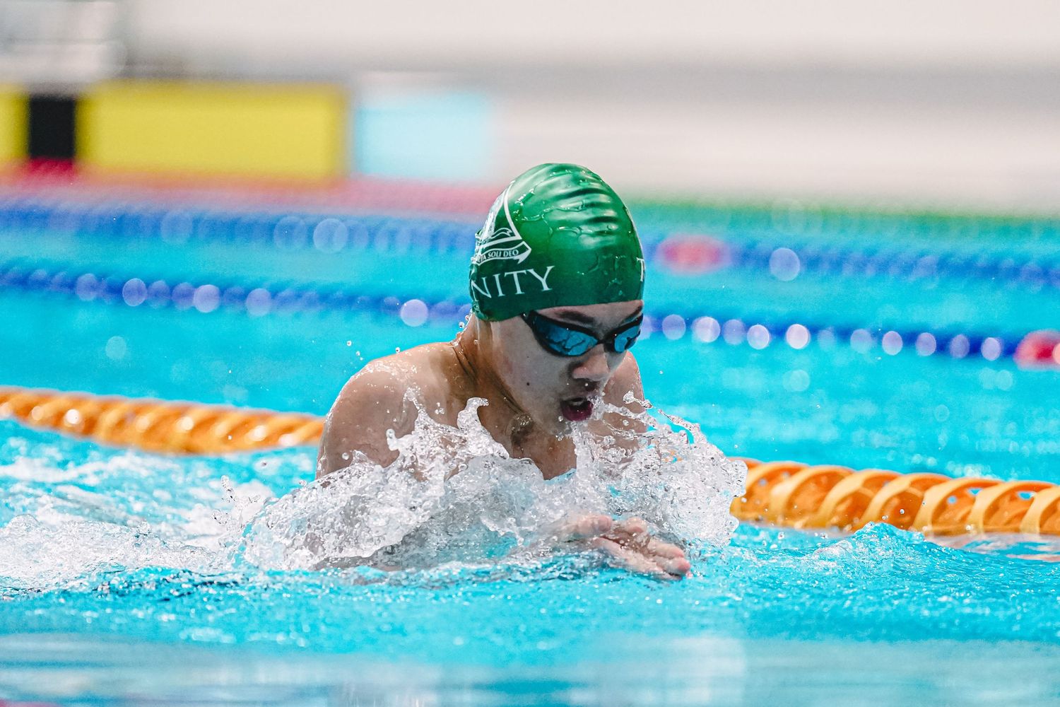 Swimmer in green cap performs breaststroke technique during competitive race in swimming pool with lane dividers.