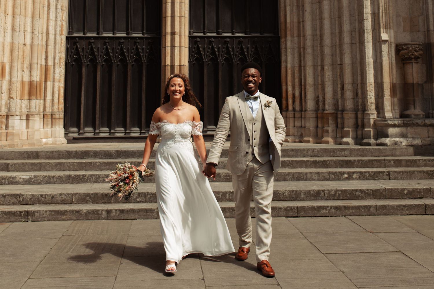A romantic wedding couple walks along the cobblestone path beside the historic York Minster cathedral on their special day.