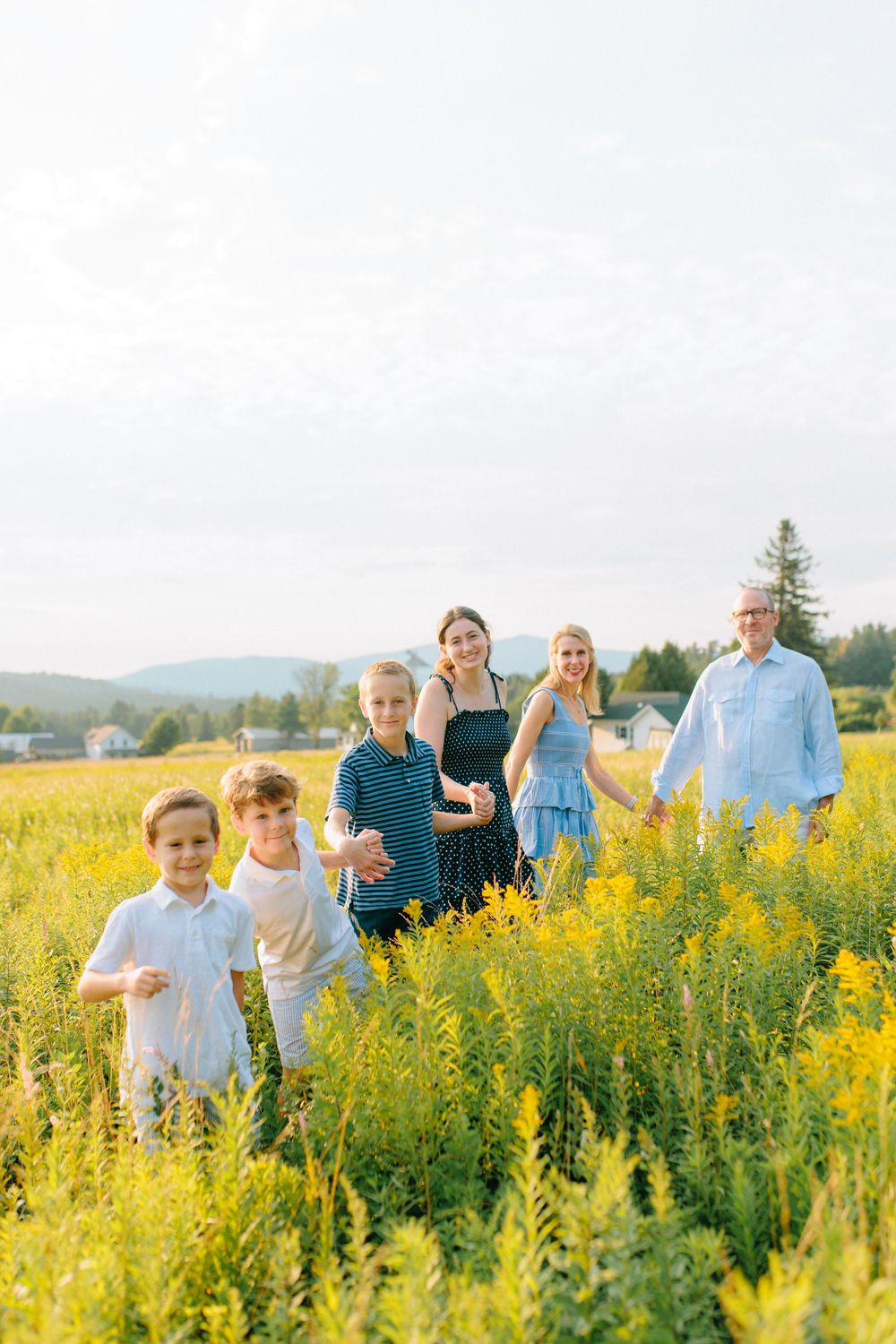 A group gathers together in a vibrant yellow wildflower field on a sunny summer day with mountains in the distance.
