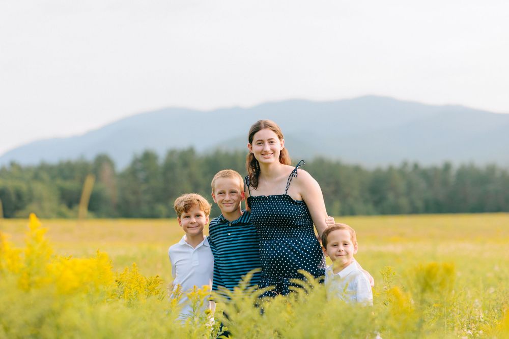 A group stands together in a yellow wildflower field with mountains and evergreen forests visible in the background.