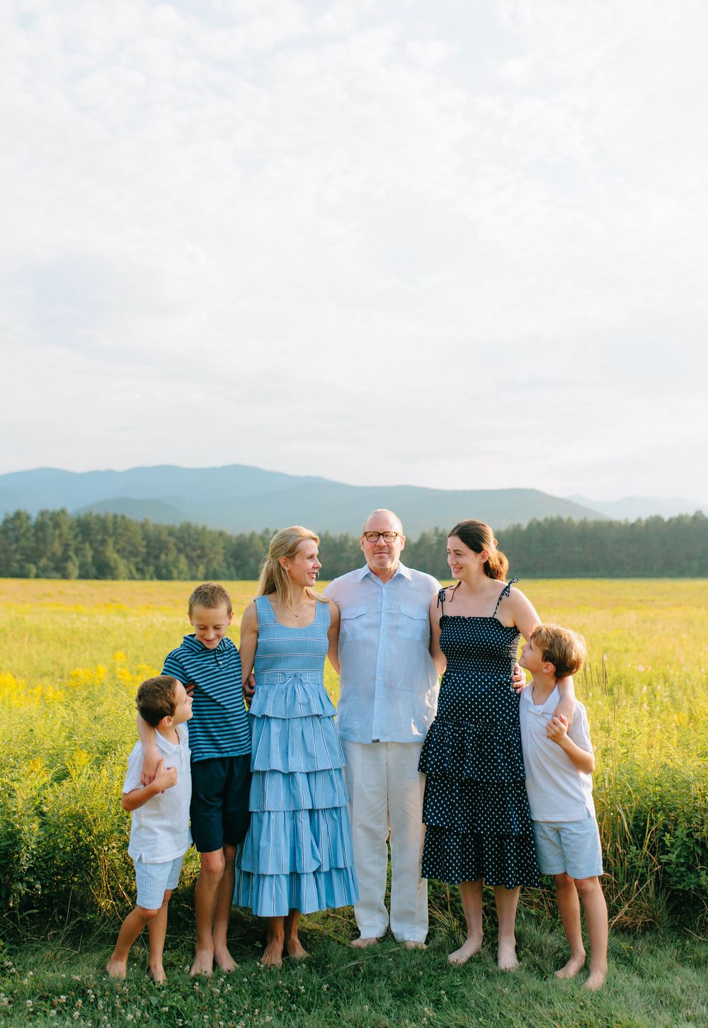 A group of people standing together against a scenic backdrop of mountains and a vibrant yellow canola field in summer.