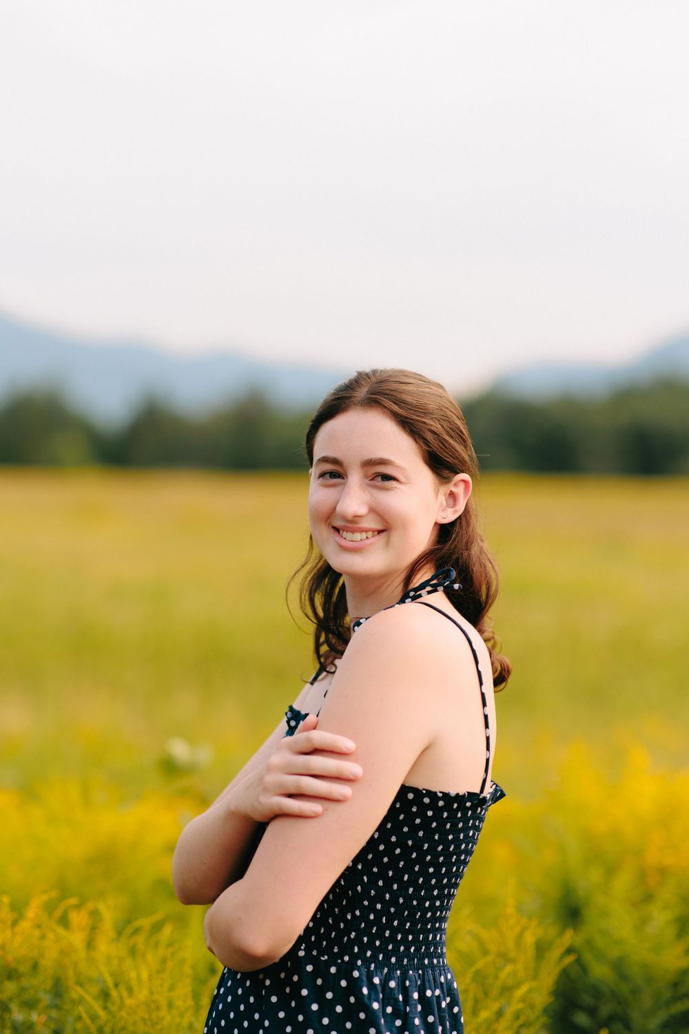 A woman in a polka dot dress laughs joyfully while standing in a vibrant yellow wildflower field.