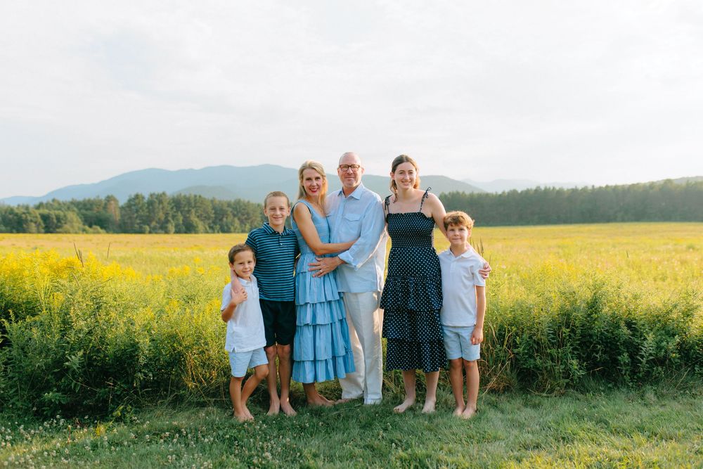 Group portrait in a scenic field with mountains and bright yellow canola flowers in the background.