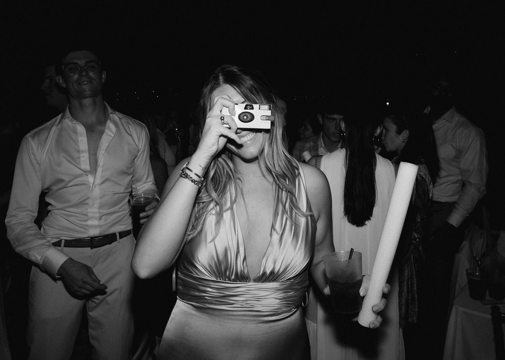 Wedding guest captures memories using a disposable film camera on the black and white reception dance floor.