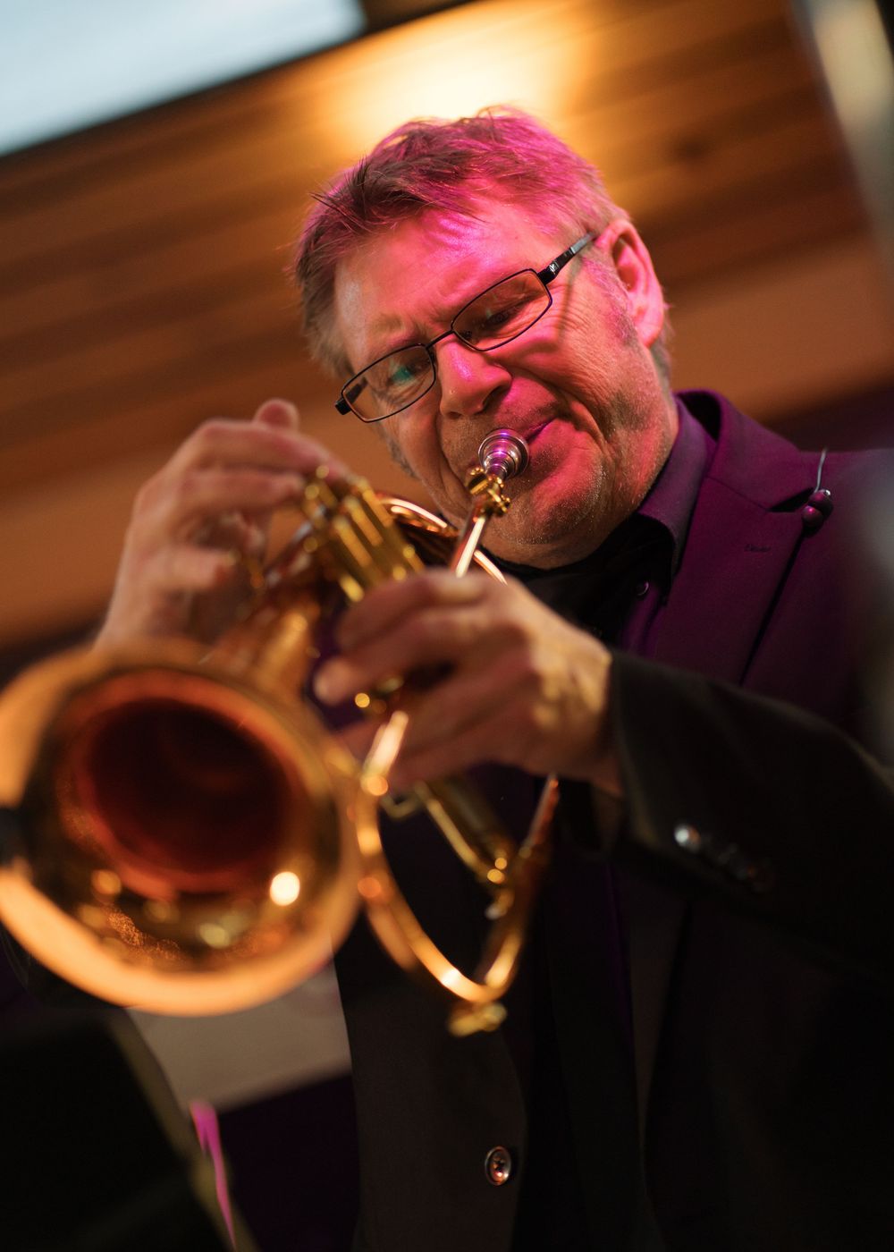 Trumpet player performs under pink stage lighting at a wedding reception, focused on his instrument.