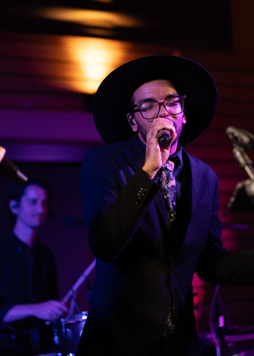 Male vocalist in black suit and wide-brim hat performs passionately on stage at a wedding reception.