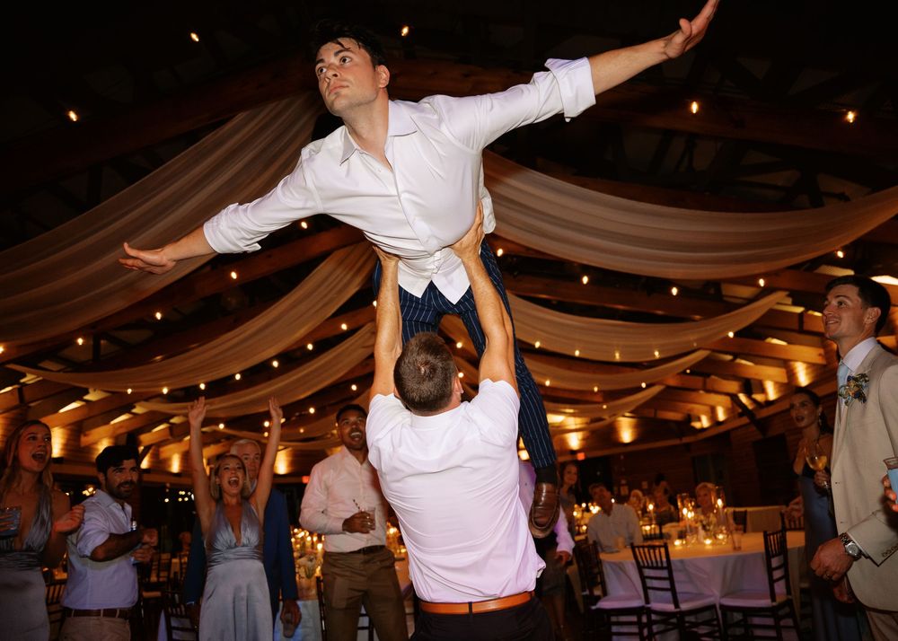 Groomsman is lifted into the air by another guest during a fun wedding reception dance.