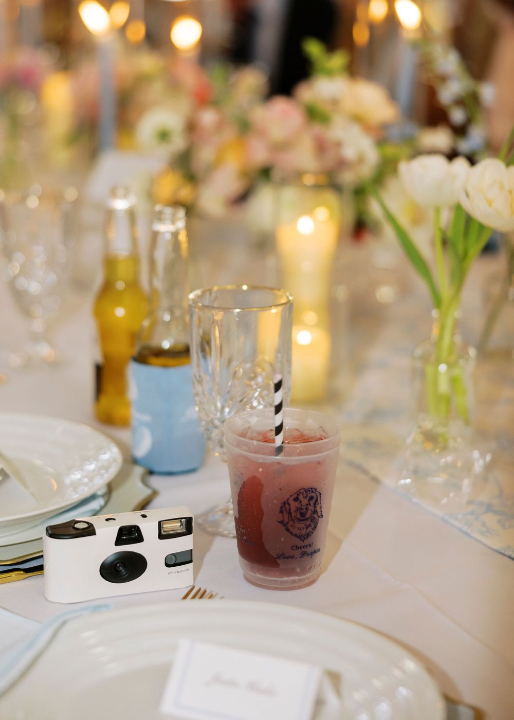 Elegant wedding reception table with disposable camera, pink frozen drink, floral arrangements, and candles.