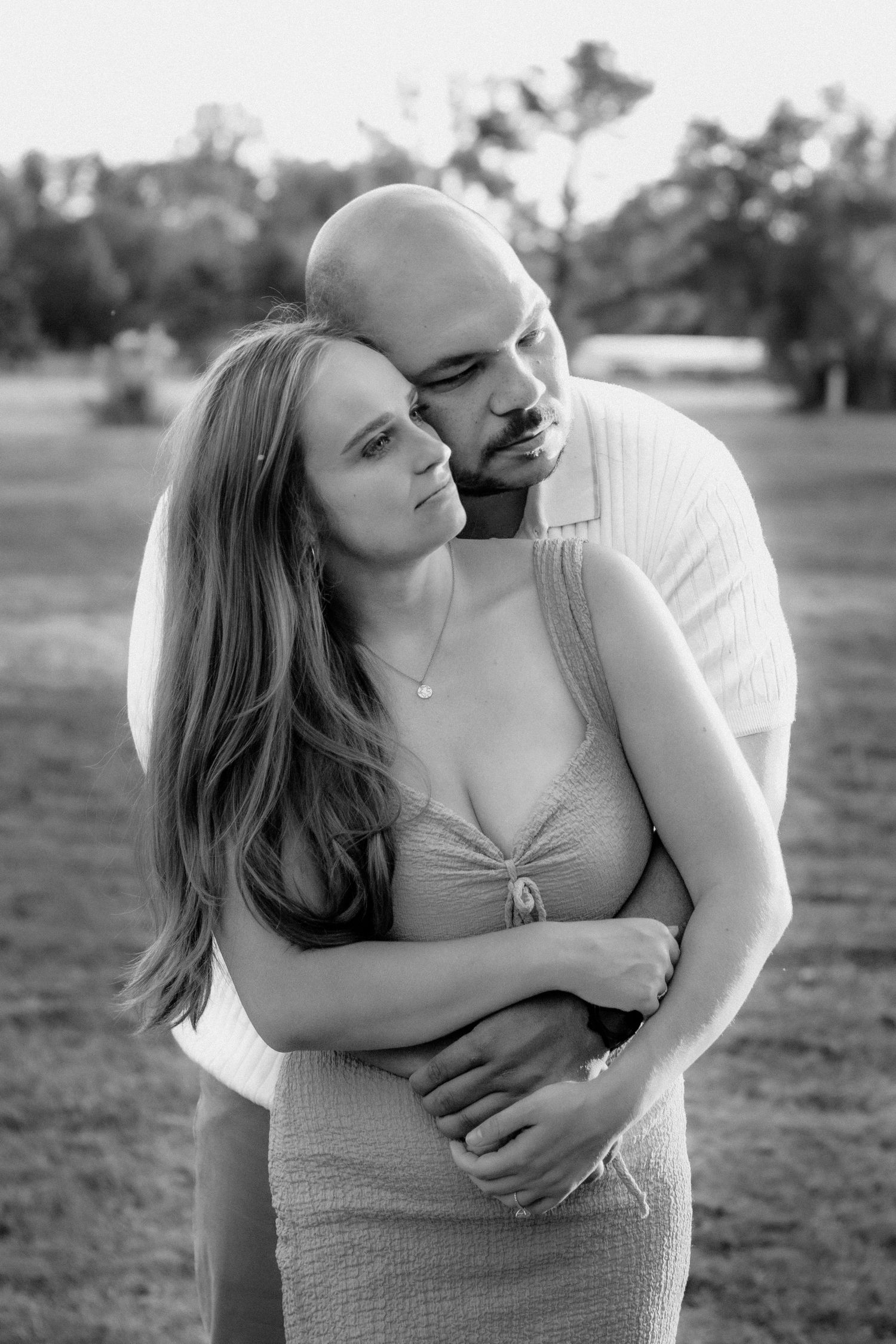 A loving couple embraces in a park during a black and white outdoor photo session.