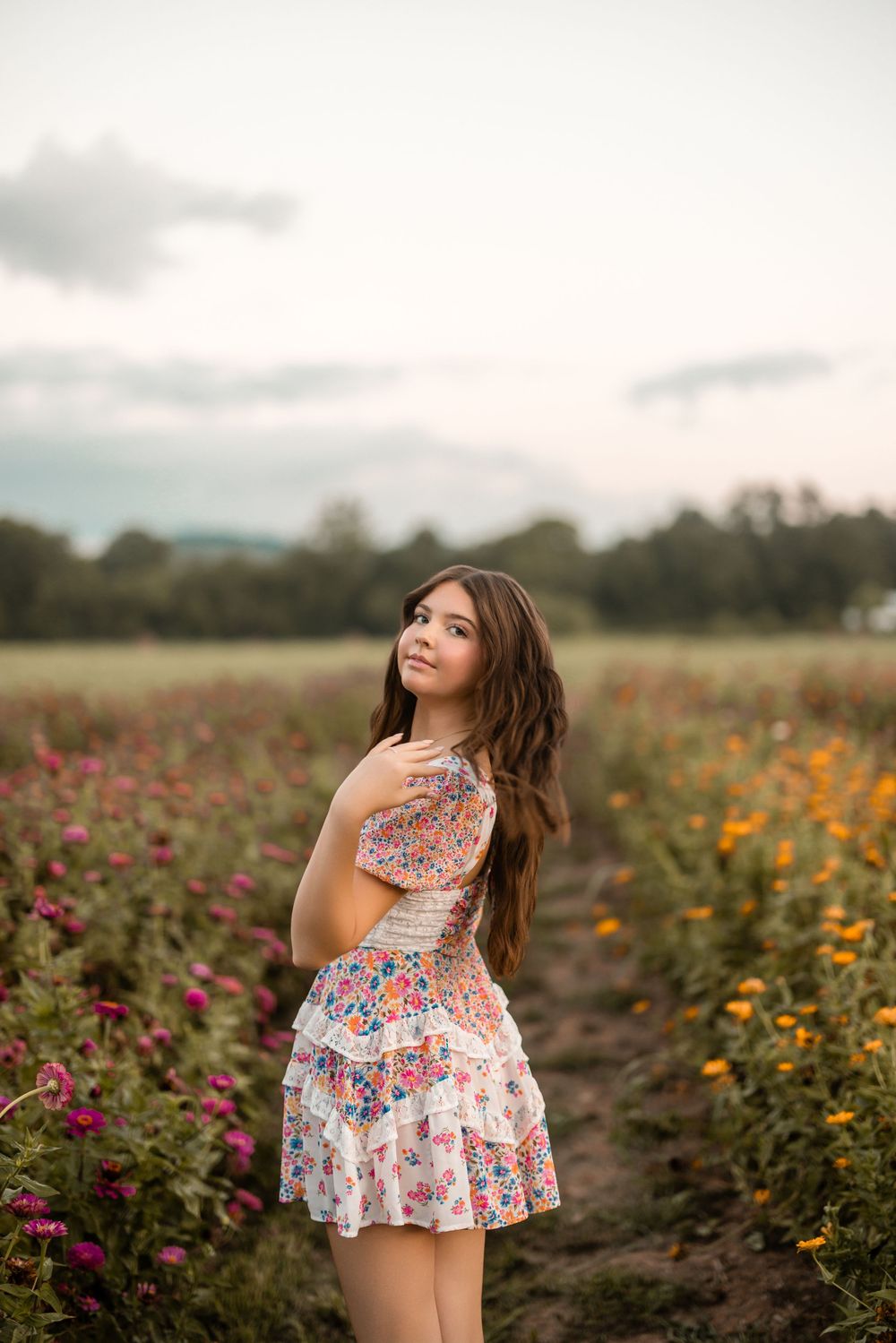 A woman in a floral dress poses gracefully in a vibrant flower field during golden hour.