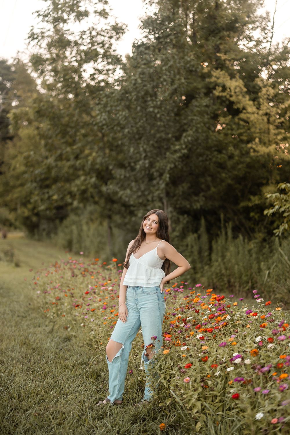 A person stands in a field of vibrant red wildflowers at sunset wearing light blue distressed jeans and a white top.