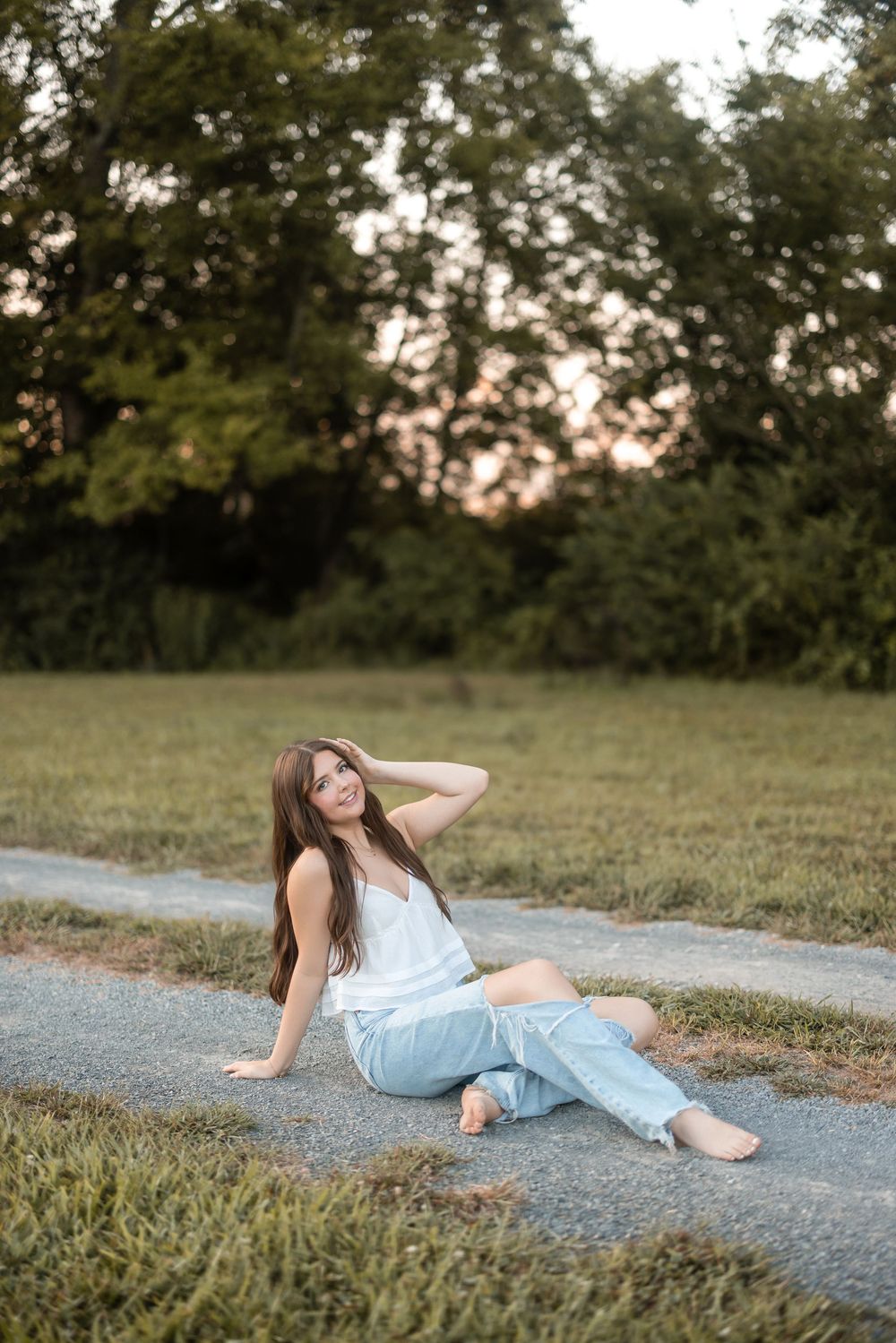 Candid outdoor portrait in casual summer wear sitting on a path with trees and sunset in background.