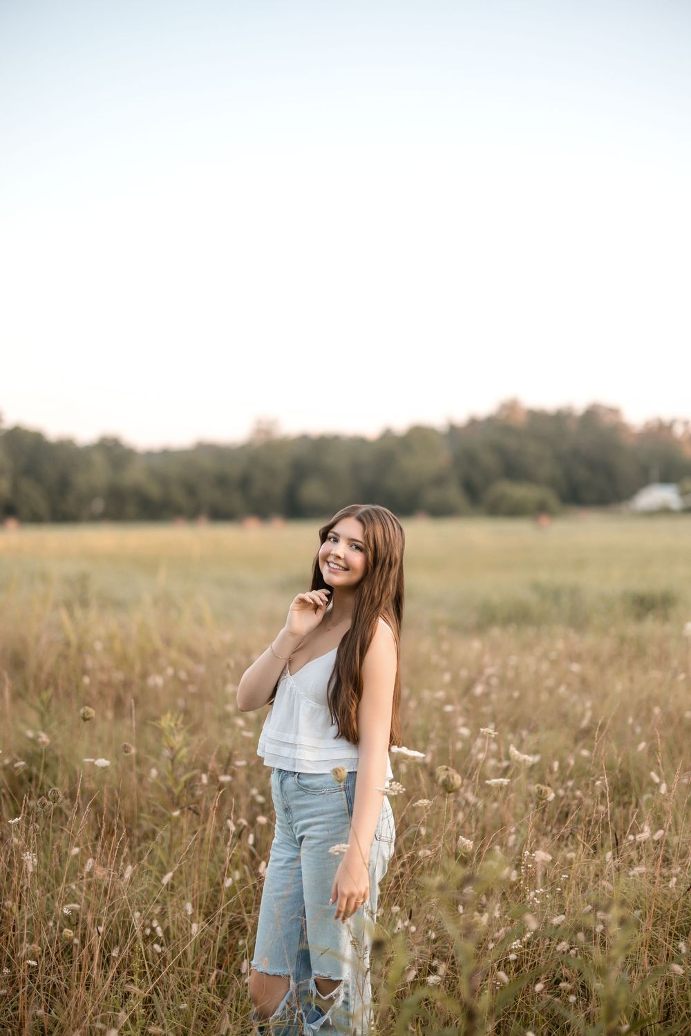 A woman in distressed jeans laughs joyfully while twirling in a golden summer meadow at sunset.