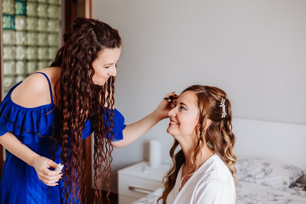 Hair styling session in progress as one person in royal blue stands helping style another in white robe.