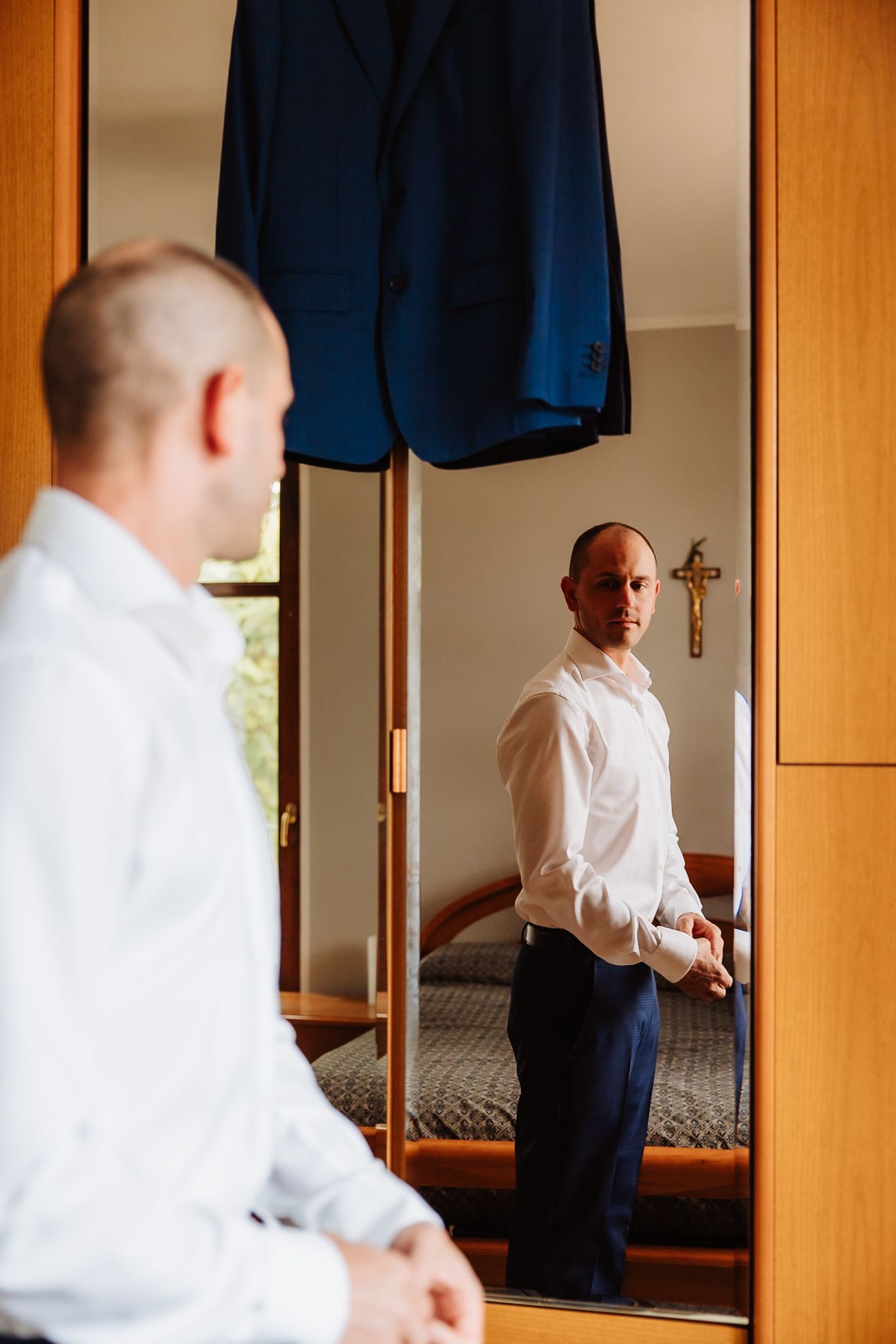 Person in formal white shirt getting dressed in front of wooden wardrobe with mirrored doors.