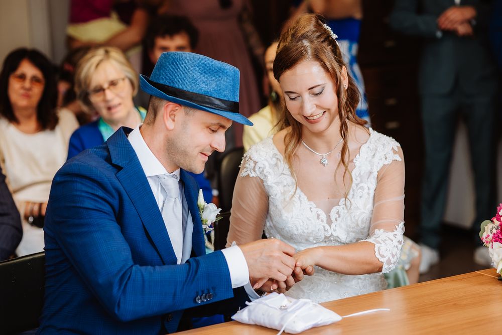 A bride and groom sign documents at a wooden table during their wedding ceremony.