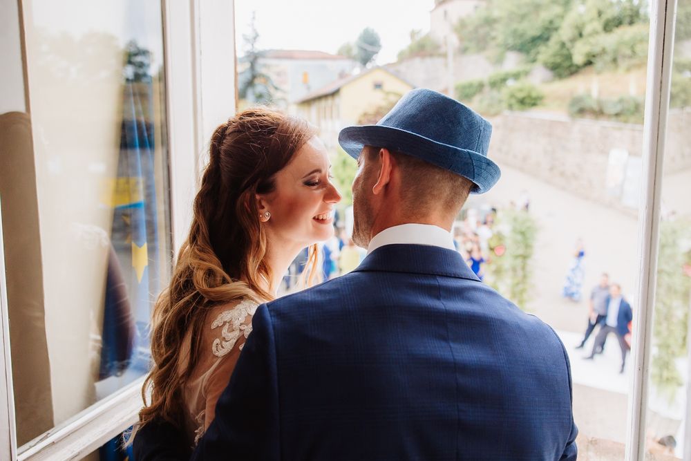 A couple shares a romantic moment by a window, with the person wearing a navy blue hat and jacket.