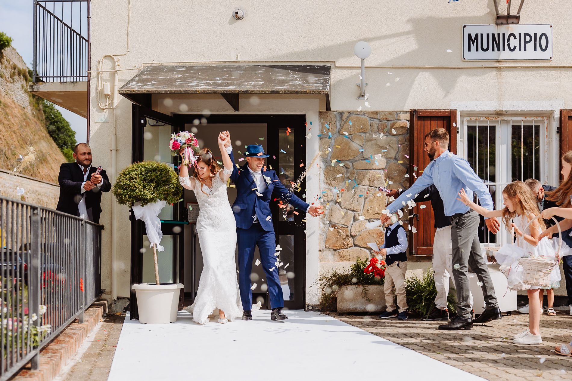 A wedding celebration outside an Italian municipio building with confetti being thrown in celebration during a summer day.