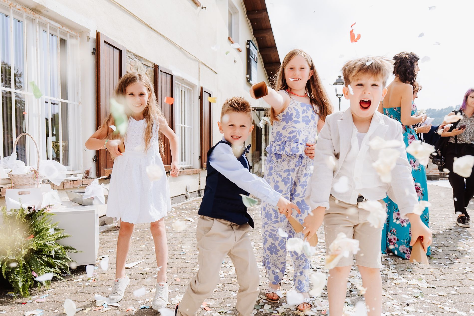 Children running and playing together along a sunny white European cobblestone street in summer clothing.