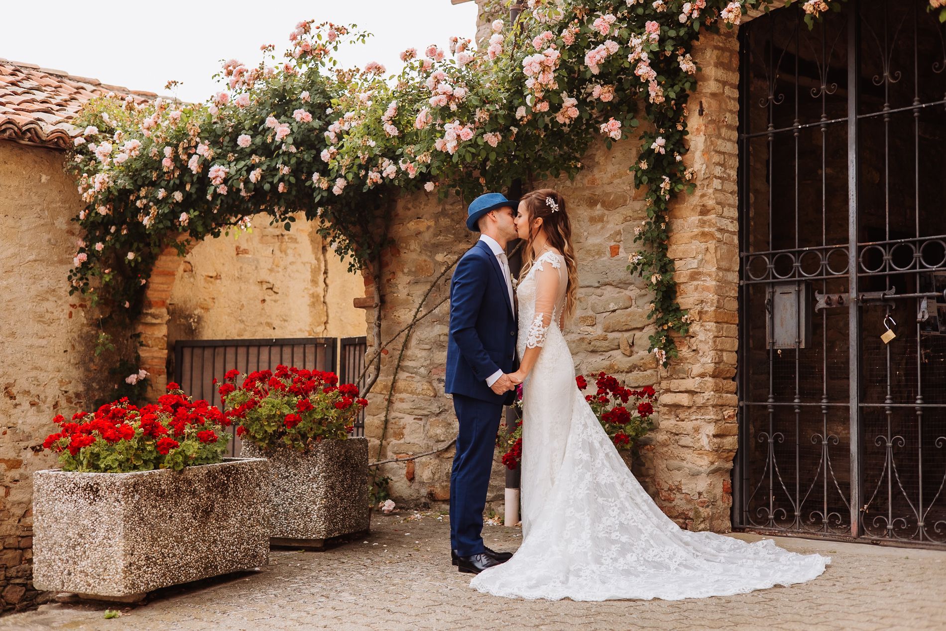 A romantic outdoor wedding scene with white floral arrangements against rustic stone walls and iron gates.
