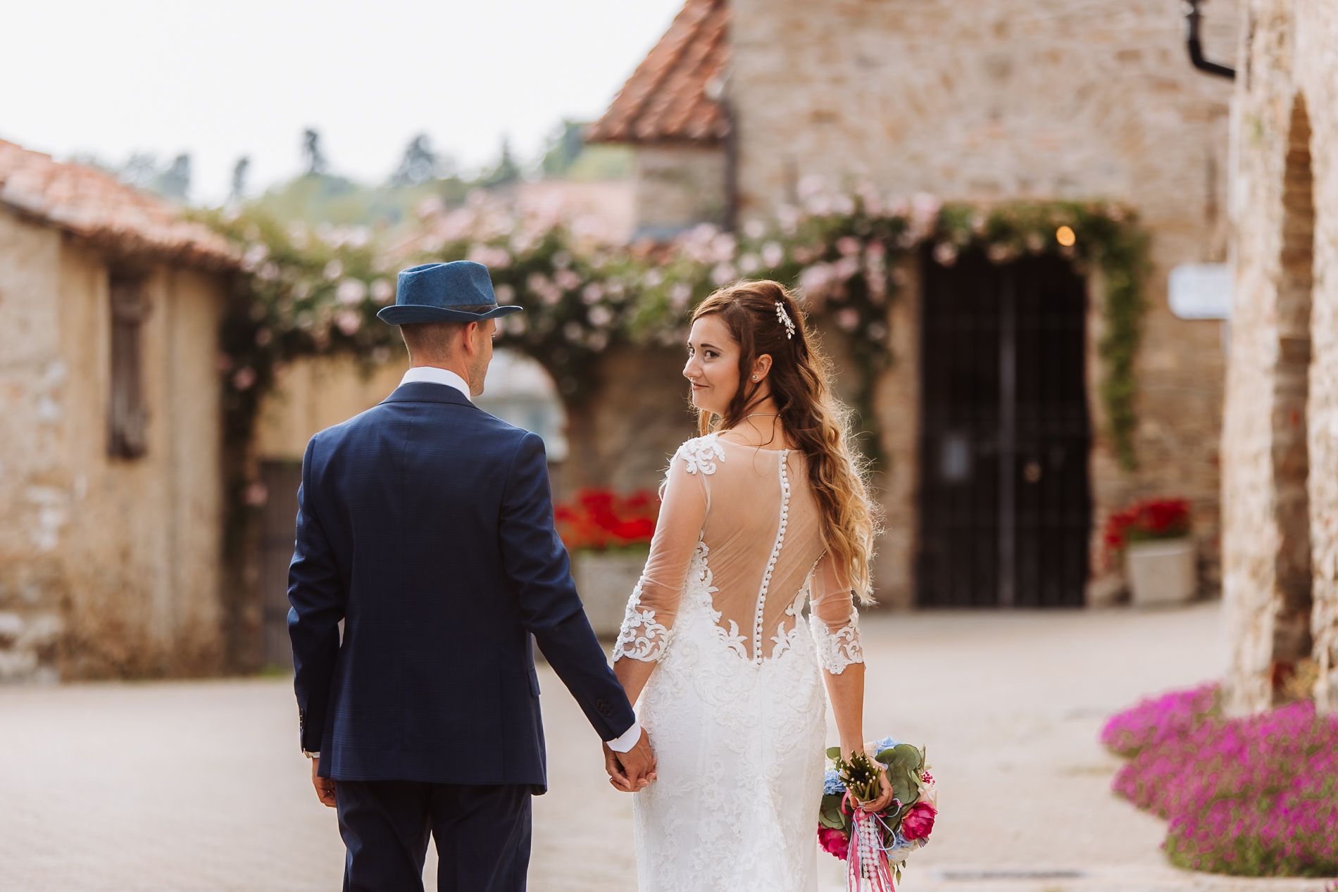 A couple walks through a charming Italian stone village with rustic buildings and flowers along the pathway.