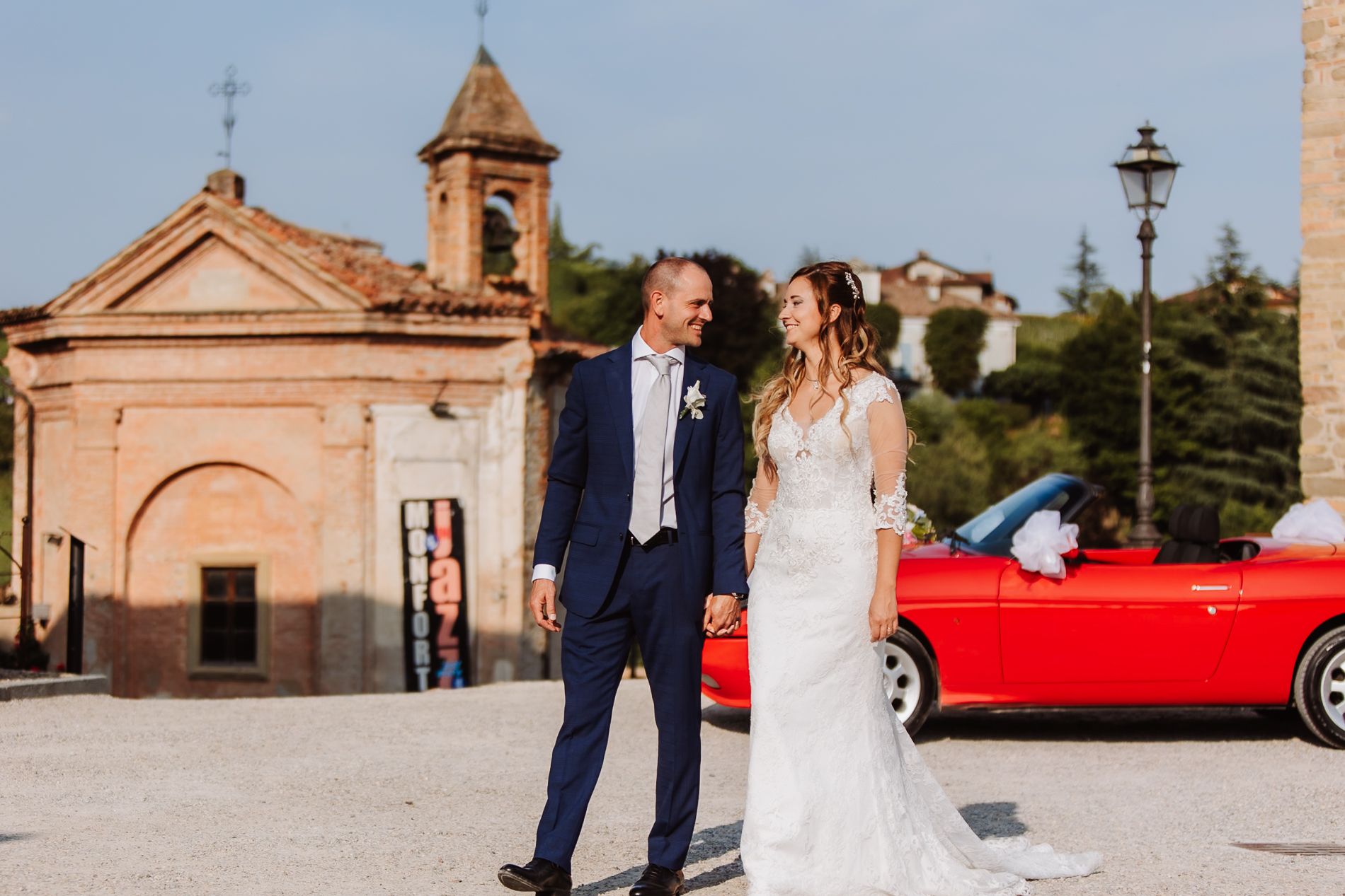 A wedding party arriving at a church in a classic red convertible car for an outdoor wedding ceremony.