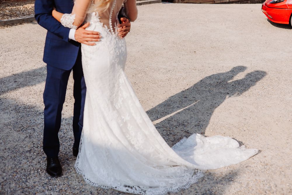 A close-up of a wedding couple showing the groom in navy suit and bride's flowing lace dress with long train.